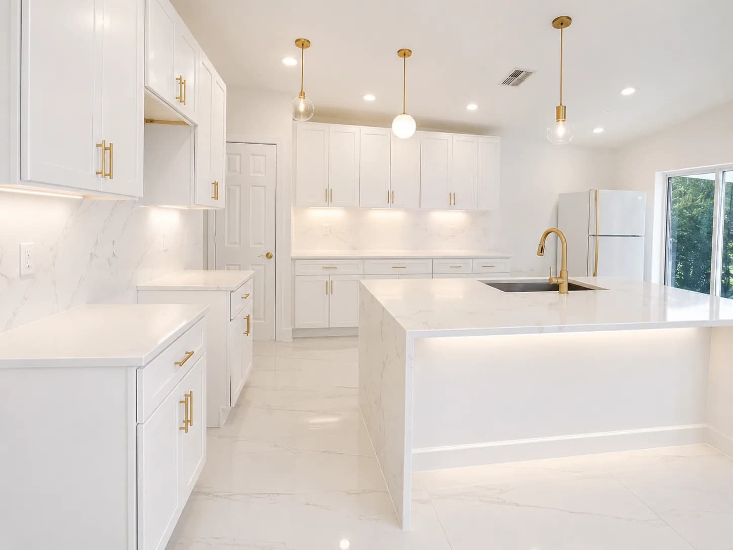 Bright luxury kitchen with white cabinetry, gold hardware, and a waterfall island